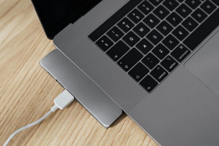 From above of gray colored contemporary netbook with usb port multiplier and white cable connected to usb hub on wooden table