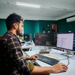 Software developer coding on dual monitors in a well-lit modern office, focused and engaged.