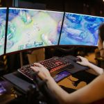 A young woman intently gaming on a multi-screen setup, showcasing vibrant gaming visuals.